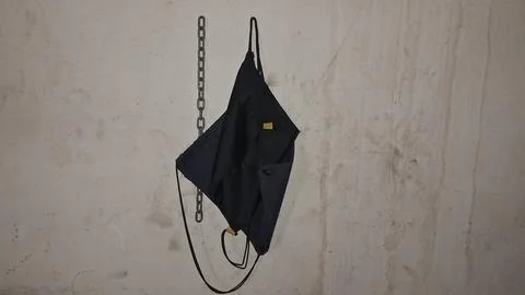 Black drawstring bag hanging from a rusty metal chain wall hook Stock Photos