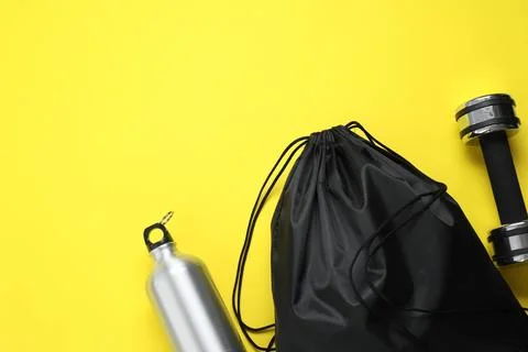 Black drawstring bag, thermo bottle and dumbbell on yellow background, flat.. Foto stock