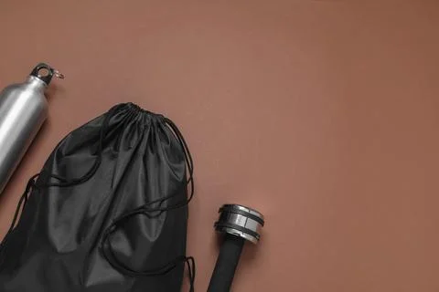 Black drawstring bag, thermo bottle and dumbbell on brown background, flat .. Stock Photos