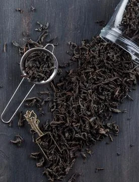 Black dry tea in strainer, jar, scoop on a wooden background. flat lay. Stock Photos