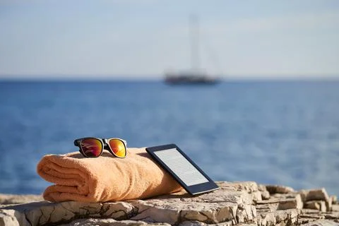 Black e-reader, orange towel and sunglasses laying on a rock near to Istrian sea Stock Photos
