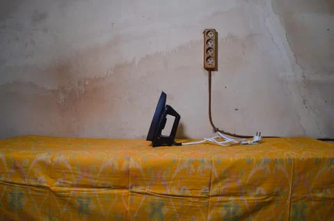 A Black Electric Iron Resting On A Table Covered With Yellow Patterned Fabric Stock Photos