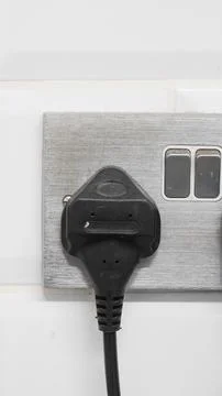 Black electrical plug connected to silver wall socket with switches nearby Foto stock