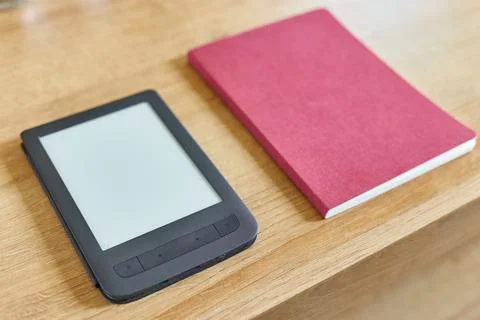 Black electronic book with empty screen and red notepad on wooden table top a Stock Photos