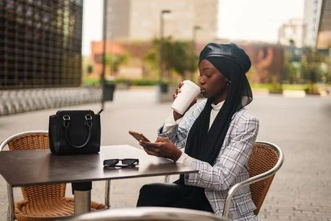 Black elegant woman drinking coffee and browsing smartphone Stock Photos