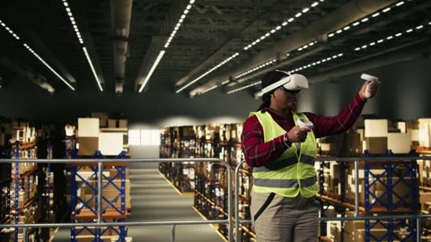 Black employee using virtual reality goggles and safety vest in warehouse Stock Footage 330209084