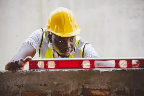 Black engineer checking wall alignment with spirit level at construction site Foto stock