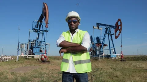 Black engineer stands against conventional pumping unit Stock Footage 226315498