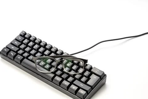 Black eyeglasses resting on compact mechanical keyboard, myopia and computer Stock Photos