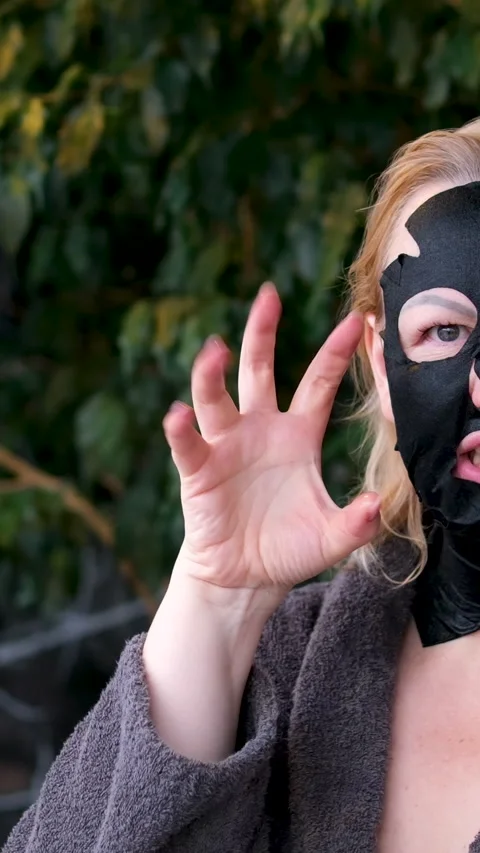 Black face mask Over shoulder mirror reflection shot of young lady with facial Stock Footage 323725968