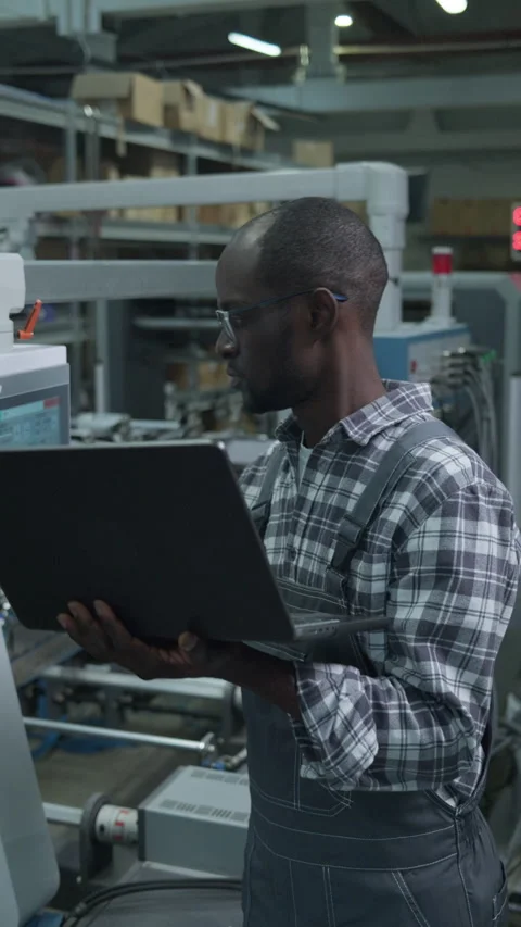 Black Factory Engineer Using Laptop to Control Automated Production Line Stock Footage 335482615