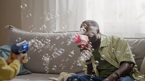 Black Father and Son Playing with Soap Bubble Guns at Home Stock Footage 345492307