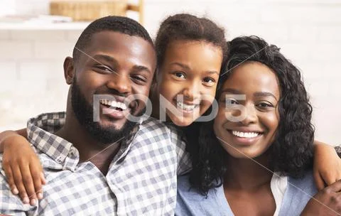 Black Father, Mother And Daughter Smiling And Looking At Camera