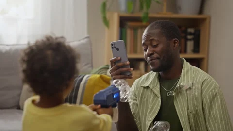 Black Father Recording Son Playing with Soap Bubbles on Smartphone Stock Footage 345490362