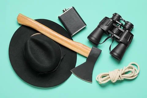 Black fedora hat, axe, flask, binoculars, and rope for outdoor adventure and  Stock Photos
