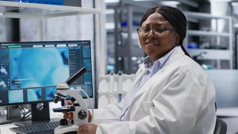 Black female expert analyzing samples in chemistry lab with microscope Stock Photos