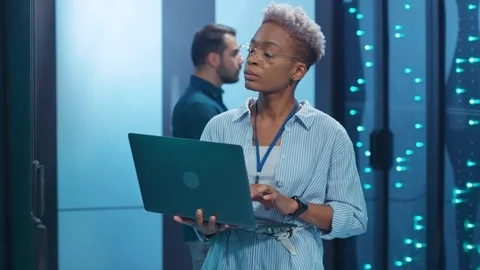Black female IT engineer upgrading hardware in rack server room corridor working Stock Footage 119842077