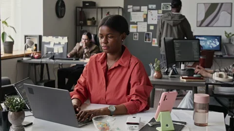 Black Female Programmer Typing on Laptop and Checking Phone in Office Stock-Footage 336713156