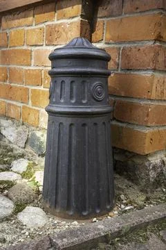 A black fire hydrant is sitting on the ground next to a brick wall Stock Photos