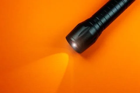 Black Flashlight and a ray of light on the orange background. Close up photo. Stock Photos