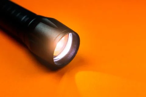 Black Flashlight and a ray of light on the orange background. Close up photo. Stock Photos