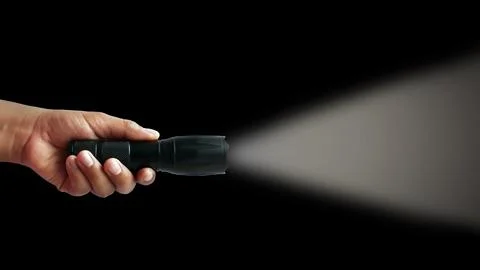 Black flashlight in human hands on a black background, including a white beam Stock Photos