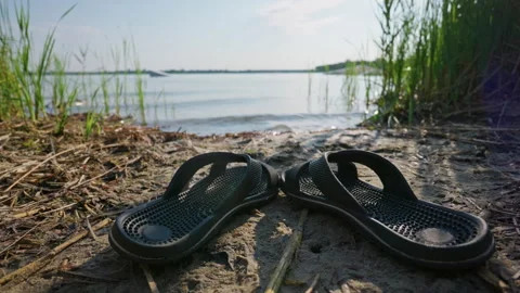 Black Flip Flops Resting on Sandy Shore Near Lake Water on Summer Day Stock Footage 342182801