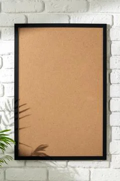 Black frame with blank board on white brick wall in room with green plant nearby Stock Photos