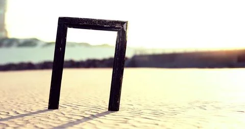 Black frame standing on sandy beach with sunlight casting long shadows Illustrazione stock