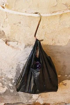 Black Garbage Bag Hanging on Rusty Hook Against Peeling Plaster Wall in Urban Se Stock Photos