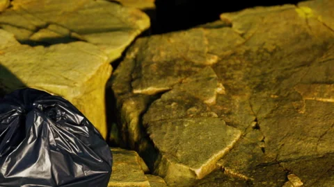 Black Garbage Bag Lying on Rough Stone Ground Outdoors During Daylight Hours Stock Footage 348597236