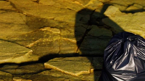 Black Garbage Bag Resting on Rough Rock Surface Under Bright Sunlight Stock Footage 348487000
