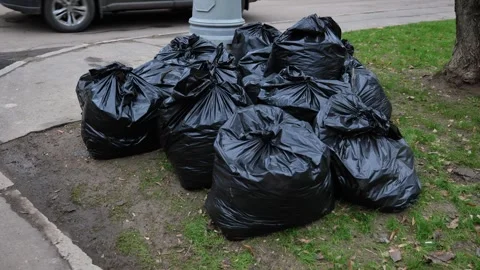 Black garbage bags piled on green grass and dirt near city street curb Stock Footage 341700862
