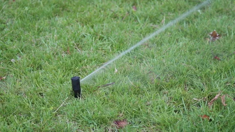 Black garden sprinkler system spraying water across green grass lawn, showcasing Vídeo Stock 340275562