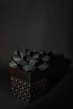 A black gift box with a geometric pattern and a black bow on a black backgrou Stock Photos