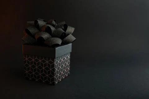 A black gift box with a geometric pattern and a black bow on a black backgr.. Stock Photos