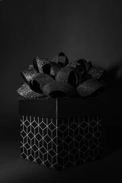 A black gift box with a geometric pattern and a black bow on a black backgr.. Stock Photos