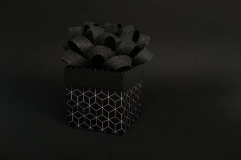 A black gift box with a geometric pattern and a black bow on a black backgrou Stock Photos