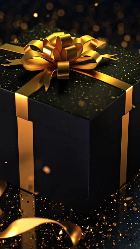 A black gift box with a gold bow on a dark surface, sprinkled with golden g.. Stock Footage 295346357