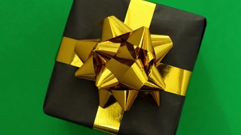 Black gift box with golden bow spins on green background. Merry Christmas Stock Footage 219459740