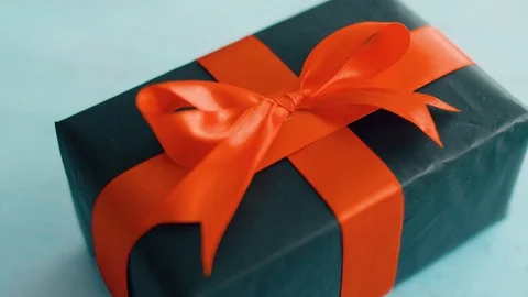 Black gift box with red silk ribbon rotating on blue wood texture.  Gift box for Stock Footage 115575552