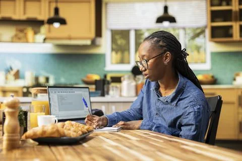 Black girl programming on laptop in a kitchen representing hybrid work in IT 写真素材