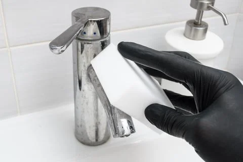 Black gloved hand cleans chrome sink mixer with melamine sponge, showing Stock Photos