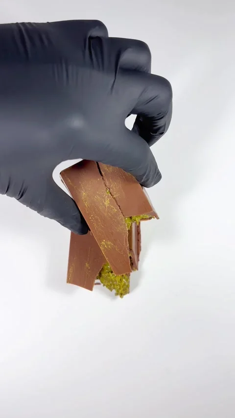 A black-gloved hand places a slice of Dubai chocolate on top of another slice Stock Footage 309453763
