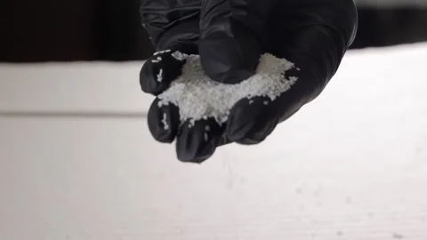 Black gloved hand pouring white plastic granules onto a pile in soft industrial Stock Footage 306406340