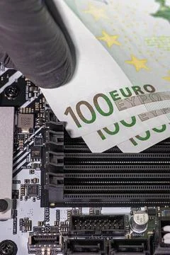Black-gloved hands inserting 100 euro banknotes into empty RAM slots on a m.. Fotos de archivo
