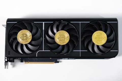 Black GPU with triple-fan cooling system and three golden Bitcoin tokens on.. Stock Photos