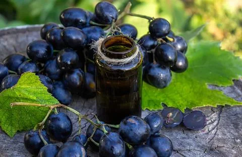 Black grape extract bottle with fresh grapes on wooden surface Stock Photos
