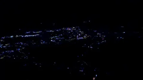 On a black-green background, flashing lights of a small city from a bird's Stock Footage 256402971