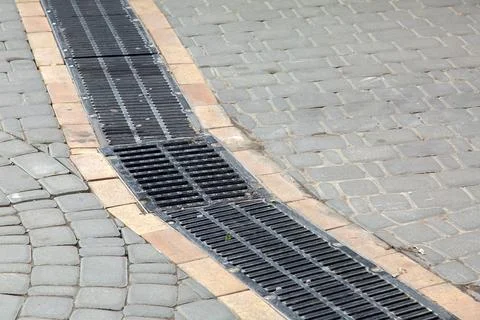 Black grille drainage system installed in the pedestrian sidewalk. Stock Photos
